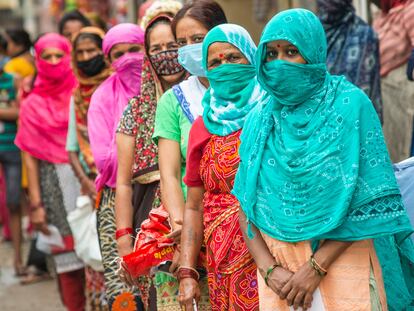 Mujeres indias esperan en una cola de reparto de raciones de comida.