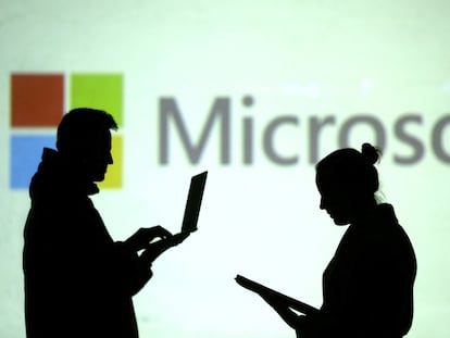 Personas con dispositivos electrónicos frente a un logo de Microsoft.