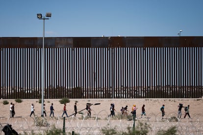 Un grupo de personas camina frente al muro fronterizo entre Ciudad Juárez (Chihuahua) y El Paso (Texas).