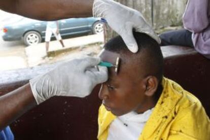 Un barbero liberiano rasura la cabeza de un cliente con guantes de látex como medida preventiva contra el virus del Ébola en Monrovia.