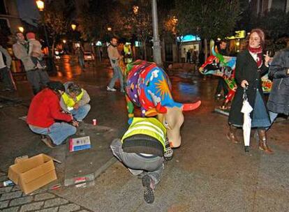 Operarios vuelven a colocar una de las vacas de la Cow Parade en la plaza de Lavapiés.