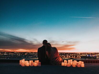 Una pareja observa el atardecer rodeada de velas.