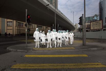 Un grupo de inspectores sanitarios camina por una calle de Hong Kong. Visten unos trajes de protección integral y llevan su cuerpo completamente cubierto. Están cerca de un mercado de aves de corral.