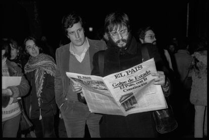 Varias personas leen la edición especial que publicó el diario EL PAÍS en los aledaños del Congreso de los Diputados la noche del golpe de Estado del 23 de febrero de 1981.