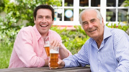 Padre e hijo disfrutando de una cerveza en una mesa de jardín.
