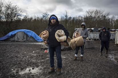 Varios migrantes kurdos recogen mantas que les ofrecen los voluntarios para soportar las bajas temperaturas del norte de Francia. Unas 3.000 personas viven desde el pasado verano en el campo de la localidad de Grande-Synthe a la espera de cruzar el canal de la Mancha y alcanzar Inglaterra.