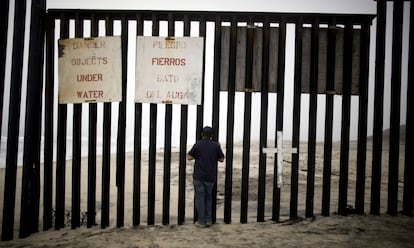 Un hombre mira hacia Estados Unidos desde los barrotes de la valla en Playas de Tijuana.