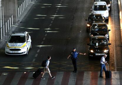 Los taxistas protestan por el modelo de servicio privatizado que representan Uber y Cabify, que está sustituyendo al servicio público del taxi. En la imagen, un policía municipal da paso a los peatones en la T4 de Madrid, donde los taxistas protestan.