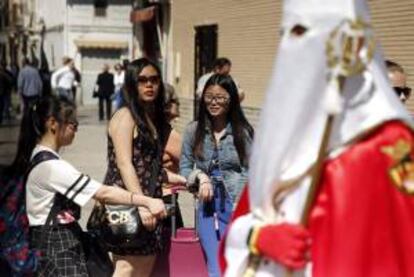Varias turistas contemplan en Viernes Santo, una de las múltiples procesiones de la Semana Santa.