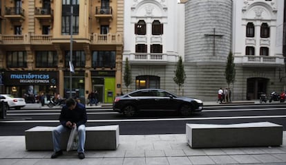 Un hombre se sienta en un nuevo banco de la Gran Vía; al fondo, el Real Oratorio del Caballero de Gracia.