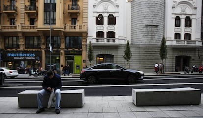 Un hombre se sienta en un nuevo banco de la Gran Vía; al fondo, el Real Oratorio del Caballero de Gracia.