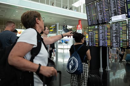 Varios viajeros miran la pantalla de los vuelos atrasados en el aeropuerto de Barcelona, este viernes.