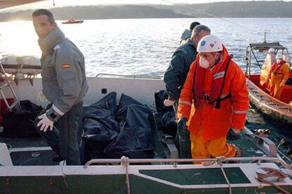 Efectivos de Salvamento Marítimo y de la Guardia Civil trasladan los cuerpos recuperados por los submarinistas del interior del pesquero naufragado.