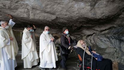 Un grupo de sacerdotes acompaña a una enferma en silla de ruedas en la entrada de la gruta del Santuario de Lourdes, en Francia, donde cada año acuden miles de peregrinos en busca de una curación para sus enfermedades.