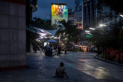 Alexander, de 16 anos, rasteja no chão em frente à fachada de um shopping center no município de Chacao, em Caracas. Ele não pode andar por um machucado no pé.