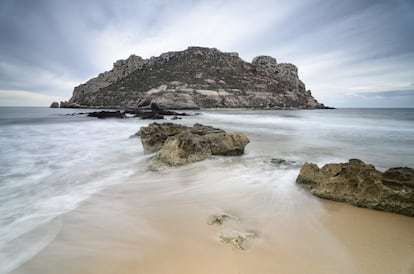 La búsqueda de valores paisajísticos encuentra su justa recompensa en esta escueta lengua de playa orientada al embarcadero del Hornillo y a las puestas de sol. Su arena es dorada y de textura fina; escueta la zona dunar; sus aguas translúcidas piden gafas de buceo. Si queremos salvar los 150 metros que nos separan de la isla del Fraile, pisaremos la punta del Cigarro, apéndice de arenisca que sirvió de cantera romana. Le sucede un hemitómbolo que, con suerte, hará que nos cubra solo hasta la cintura. En su cara oculta, la isla es un acantilado cortado a pico. Hay restos de una factoría de salazones tardorromana, hornos de yeso y cal (1879), viviendas de principios del siglo XX y una cantera de tierra láguena, usada para impermeabilizar techumbres. Y, sí, una urbanización que afea el entorno.