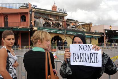 Una marroquí con un cartel que dice "no a la barbarie", junto a dos jóvenes turistas ayer ante el café Argana.