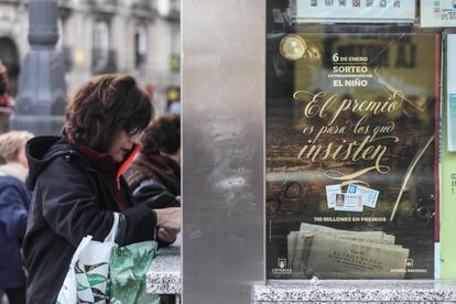 Una mujer compra lotería en una administración de Madrid, junto al cartel promocional del sorteo de este 2018, que repartirá 700 millones de euros en premios. Son 70 millones de euros más que el año pasado, cuando la Sociedad Estatal de Loterías y Apuestas del Estado (Selae) destinó a premios 630 millones. La dotación del primer premio del sorteo es de 2.000.000 de euros por serie; la del segundo, de 750.000 euros, y la del tercero, de 250.000 euros.