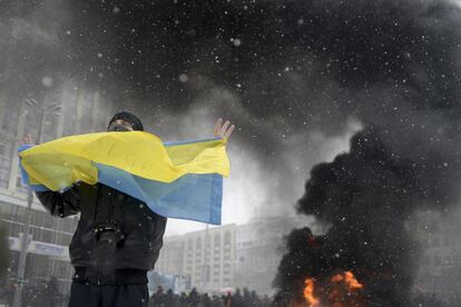 Un hombre sostiene una bandera de Ucrania ante una columna de humo provocada por los cócteles molotov lanzados durante los enfrentamientos entre la policía y manifestantes pro-europeos en Kiev 22 de enero 2014. 