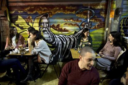 Clientes de una cafetería charlan junto a un grafiti de Moisés pintado por el artista callejero Solomon Souza.
