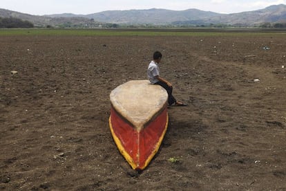 Un niño permanece sentado sobre un bote en el terreno seco sobre el que estuvo el lago Atescatempa.