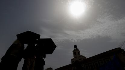 Varias personas se protegen del sol mientras cruzan la Puerta del Sol de Madrid durante una de las olas de calor del verano de 2023.