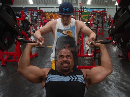 Un hombre levanta pesas ayudado por un instructor en un gimnasio en el Estado de México.