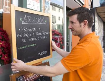 Un empleado del café coloca el aviso que prohíbe entrar con pijama.