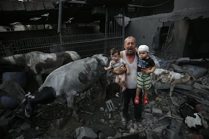 Un hombre sostenía en sus brazos a dos niños heridos, este domingo, entre ganado y edificios afectados por ataques israelíes en el campo de refugiados de Nuseirat.