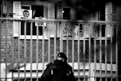 Un policía municipal hace guardia frente al piso de Lamín, un emigrante procedente de Mali, momentos antes de su desahucio en el madrileño barrio de Usera, mientras activistas de la Plataforma de Afectados por la Hipoteca hacen el signo de la victoria. España, 18 de enero de 2012.