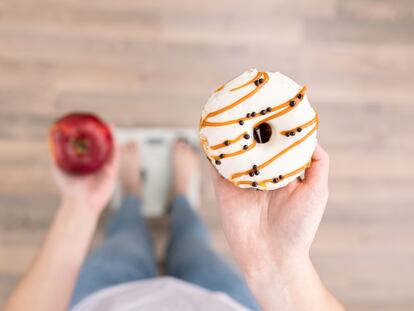 A woman stands on the scales, holds a donut and an apple in her hands, top view - Novo Nordisk - El peso de la salud 2