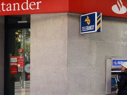 Una mujer retira dinero de un cajero automático en una oficina de Banco Santander.