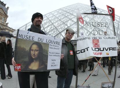 Trabajadores del Louvre en huelga exhiben sus pancartas ante la Pirámide de acceso al museo.