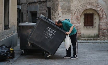Un hombre busca en un contenedor de basura en una calle de Segovia en julio.