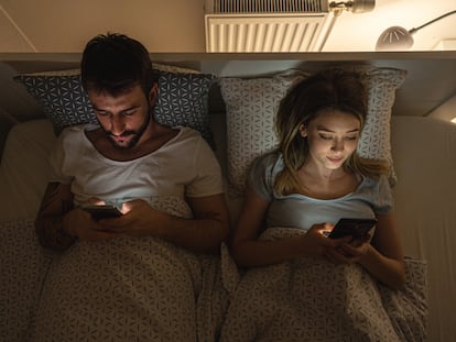 A couple looking at their mobile phones in bed.