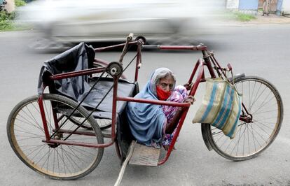 Una anciana con mascarilla espera con su silla de ruedas en la calle, en el este de India.
