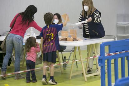 Una mujer deposita su voto, acompañada de dos menores, en el polideportivo de Manzanares el Real.