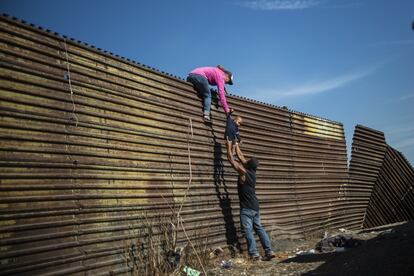 Una familia de migrantes trepa la valla fronteriza entre México y Estados Unidos, cerca del cruce fronterizo de El Chaparral, en Tijuana.