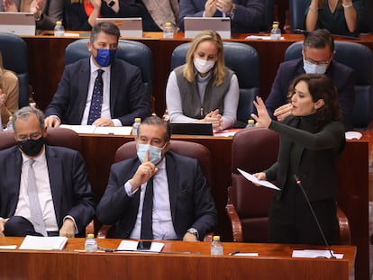 La presidenta de la Comunidad de Madrid, Isabel Díaz Ayuso (de pie), durante la intervención. En primer término, a su lado, el portavoz del Gobierno, Enrique Ossorio (a la izquierda) y el consejero de Presidencia, Enrique López, que pide silencio a la oposición.