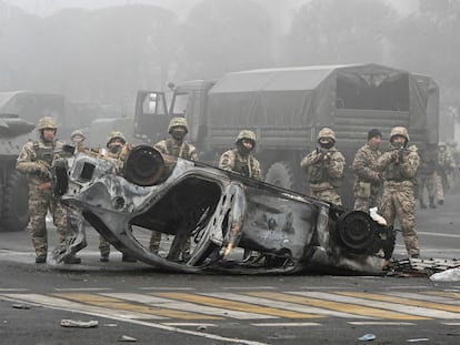 Soldados kazajos, este jueves, detrás de un automóvil calcinado durante las protestas por el alza del precio de los combustibles, en Almaty (Kazajistán).