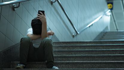 Un adolescente sentado solo llora con un teléfono móvil en la mano, en una imagen de archivo.