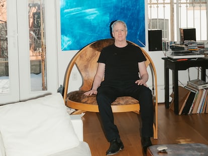 Tony Oursler, sentado en su salón en la silla que intercambió con su amigo el artista Richard Artschwager. En la pared, el espejo azul obra de Oursler.