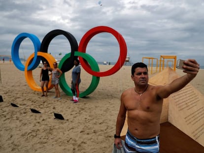 Homem faz um selfie em frente ao s&iacute;mbolo das Olimp&iacute;adas em Copacabana.