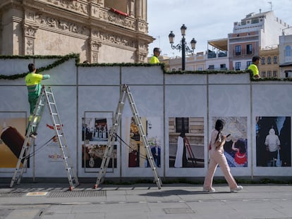 Tres operarios preparan los palcos de la Semana Santa, decorados con una exposición de fotografías, en la Plaza de San Francisco, Sevilla.
