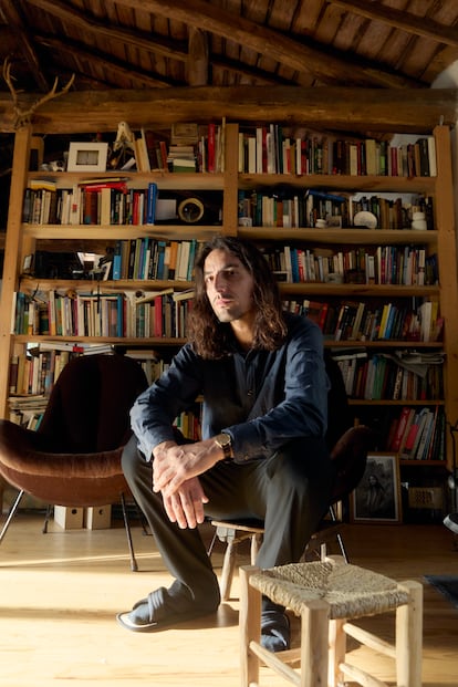 Carlos Risco en su salón, junto al muro de libros y los dos butacones que llegaron a él a cambio de ocuparse de sus dos gatos. 