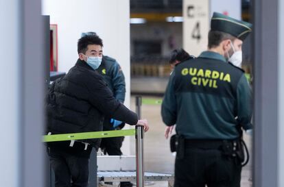 Un agente de la Guardia Civil con un pasajero que llega al aeropuerto Adolfo Suárez Madrid-Barajas procedente de un vuelo de Chongqing (China).