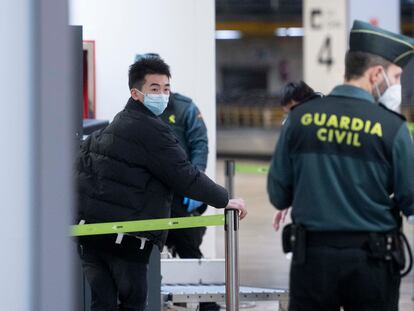 Un agente de la Guardia Civil con un pasajero que llega al aeropuerto Adolfo Suárez Madrid-Barajas procedente de un vuelo de Chongqing (China).