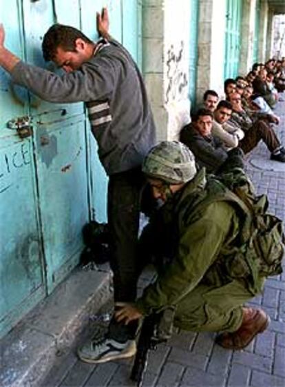 Un soldado israelí cachea a un palestino detenido en Hebrón.
