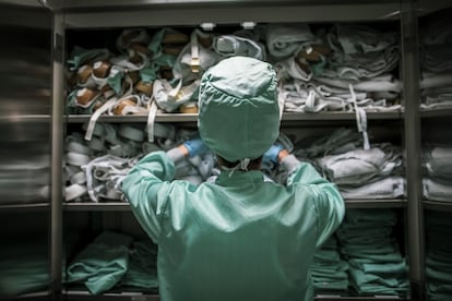 Una persona recogiendo material sanitario en un armario donde hay guardados gorros, guantes, bata, calzas y mascarillas.