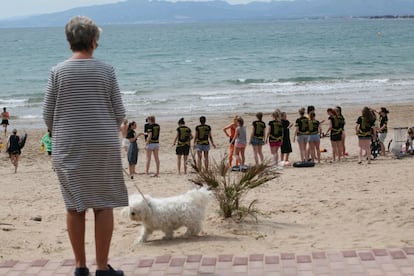 Una dona passeja el gos davant els estudiants que fan les primeres activitats esportives a la platja.